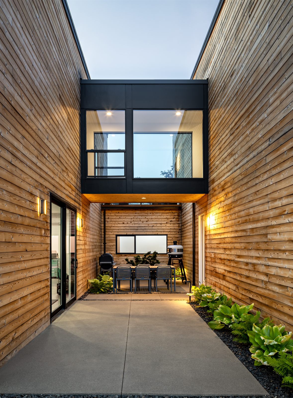 Cedar-clad courtyard framed by a glass bridge, glowing at twilight