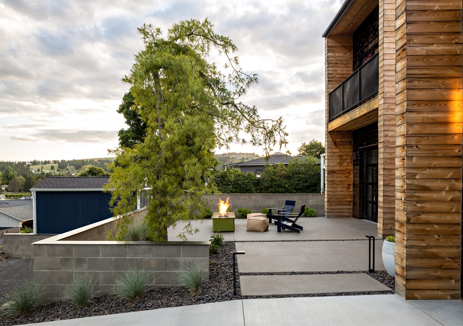 Evening patio and fire table beneath a weeping conifer